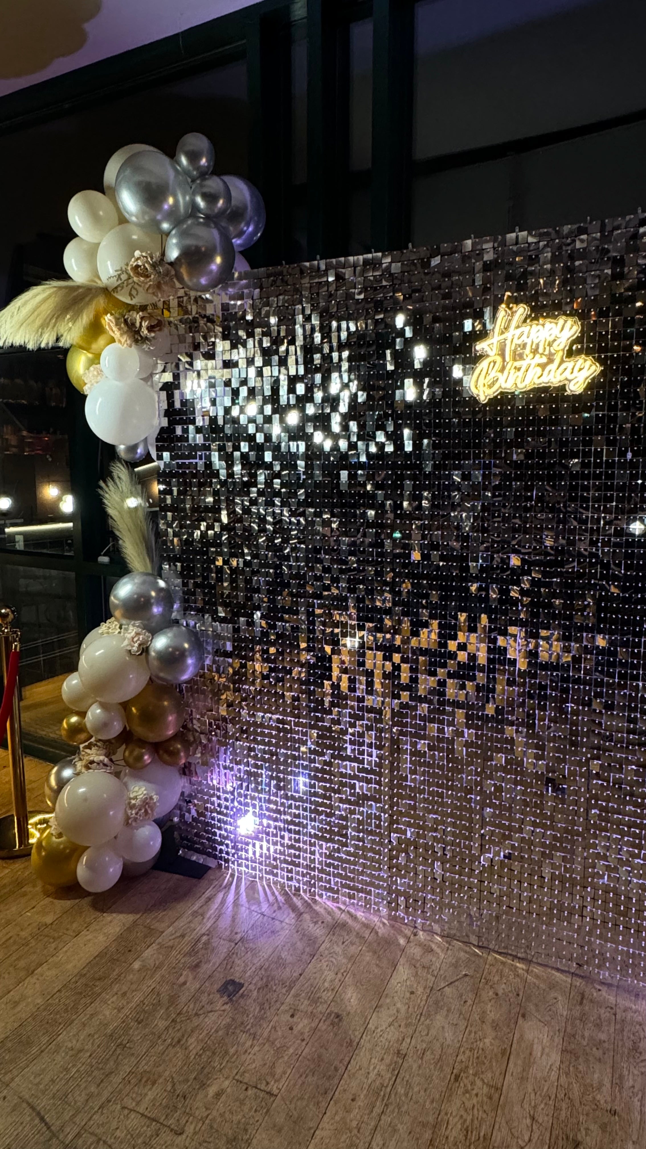 Elaborate party backdrop featuring a sparkling sequin wall and balloon arch with a 'happy birthday' led sign. enhancing the special occasion.